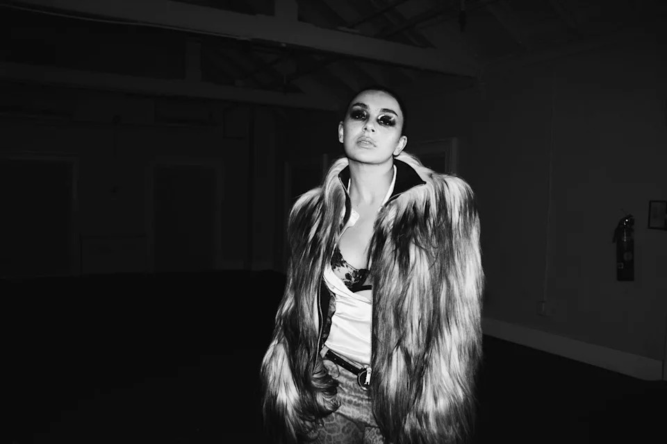 Person wearing a fur coat in a dimly lit indoor space.