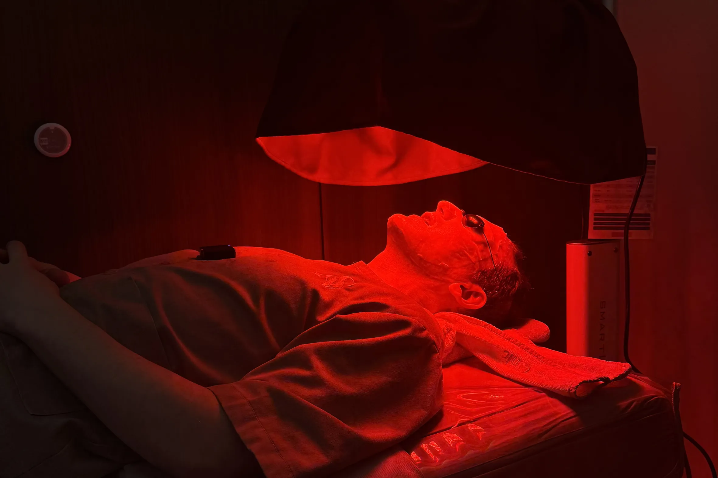 A man lying on his back receiving red light therapy on his face.