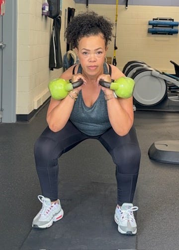 Person performing a squat exercise with dumbbells in a gym.