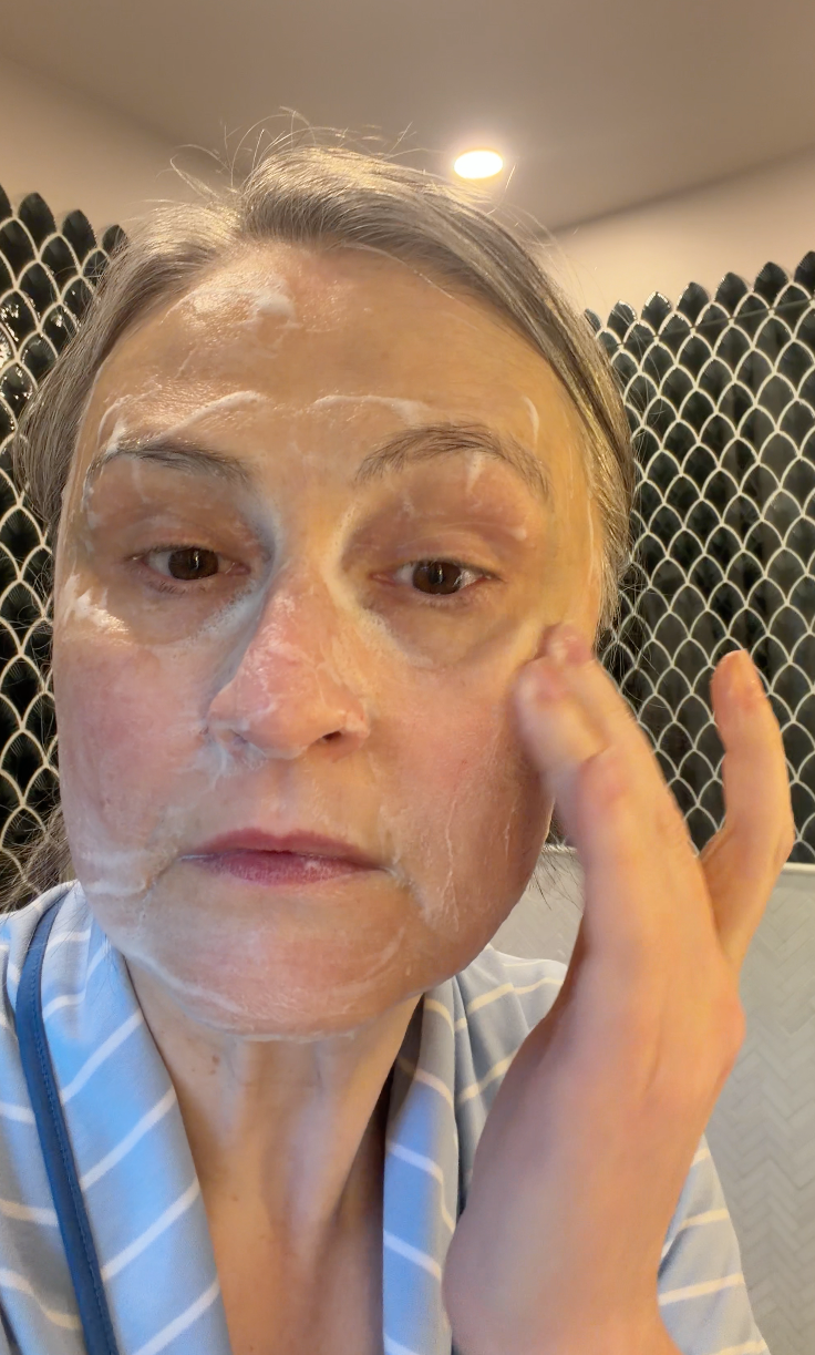 Person applying makeup in a bathroom setting.