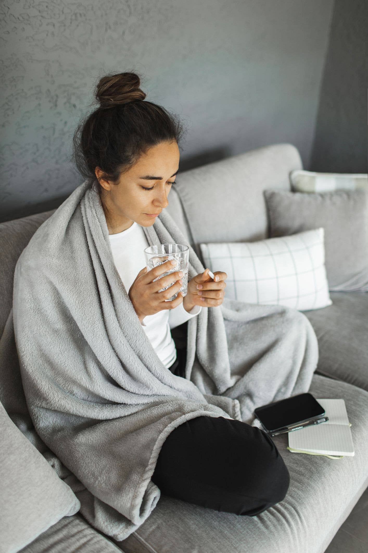 Woman with fever sitting on couch. Covered in plaid and takes antipyretic pills.