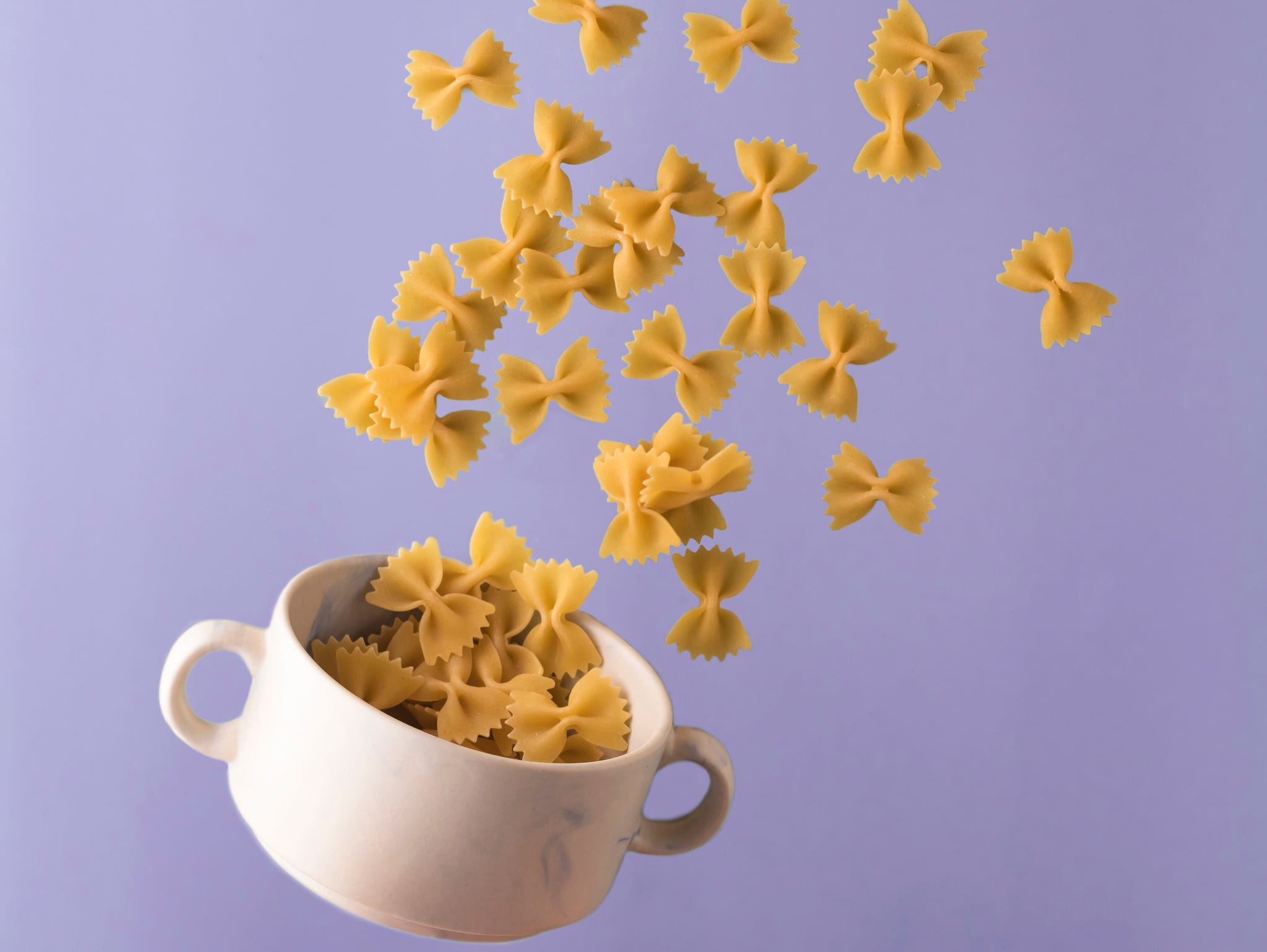 italian pasta pattern on a bright blue background. bow tie bowl with pasta. flying food concept. levitation. vertical position