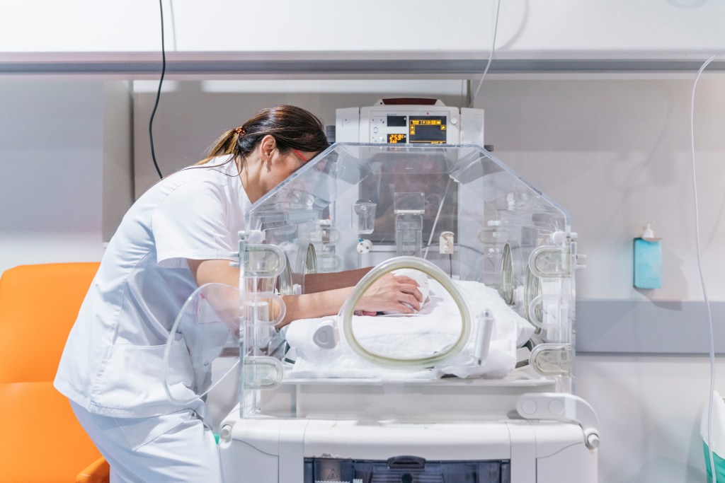 Female doctor examining a newborn baby in an incubator.
