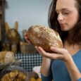 Woman holding and smelling a loaf of dark bread while learning that color does not always mean whole grain