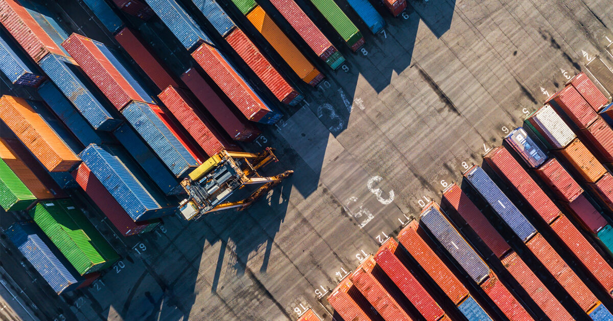 Aerial view of container port, just showing the dock with containers and a forklift.