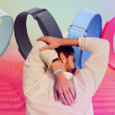 A Fitbit Air user faces away as they reach behind them. A band is visible on their left wrist. In the background are four Fitbit Airs in the four available colors.