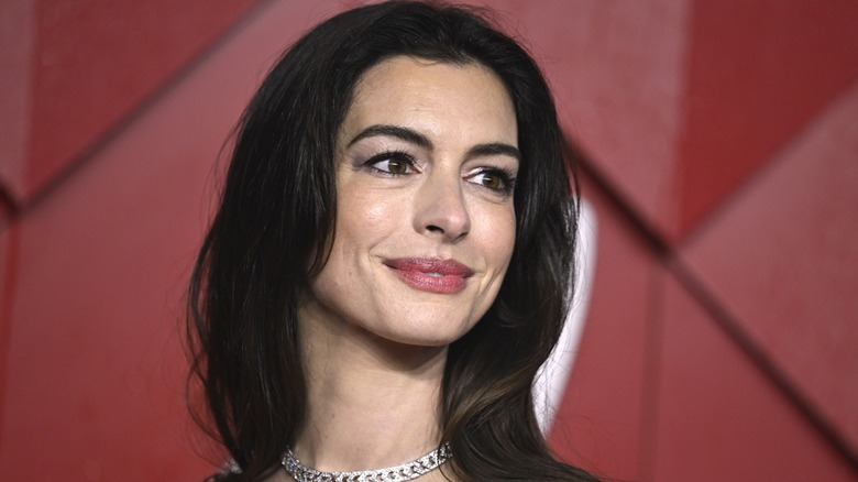 Anne Hathaway on the red carpet looking to the side in front of a red background