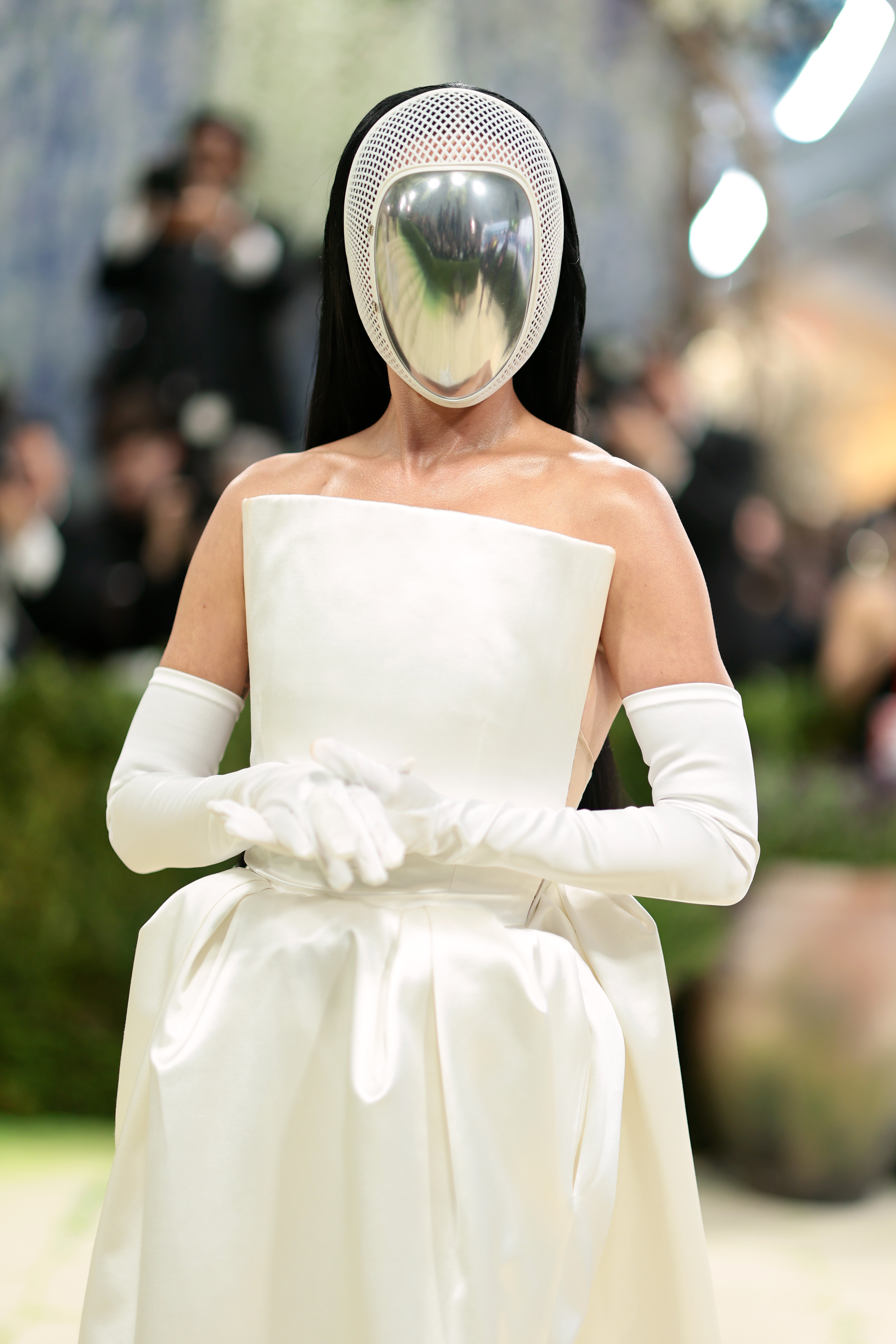 a woman in a white gown with white gloves and her face blocked by a silver mask