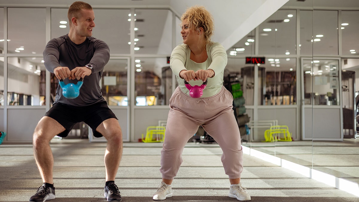 woman performing kettlebell exercise with personal trainer in gym