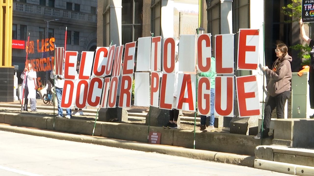 Protesters hold sign which reads "Welcome to Cle Dr. Plague" outside The City Club of Cleveland during a forum featuring Robert F. Kennedy, Jr.