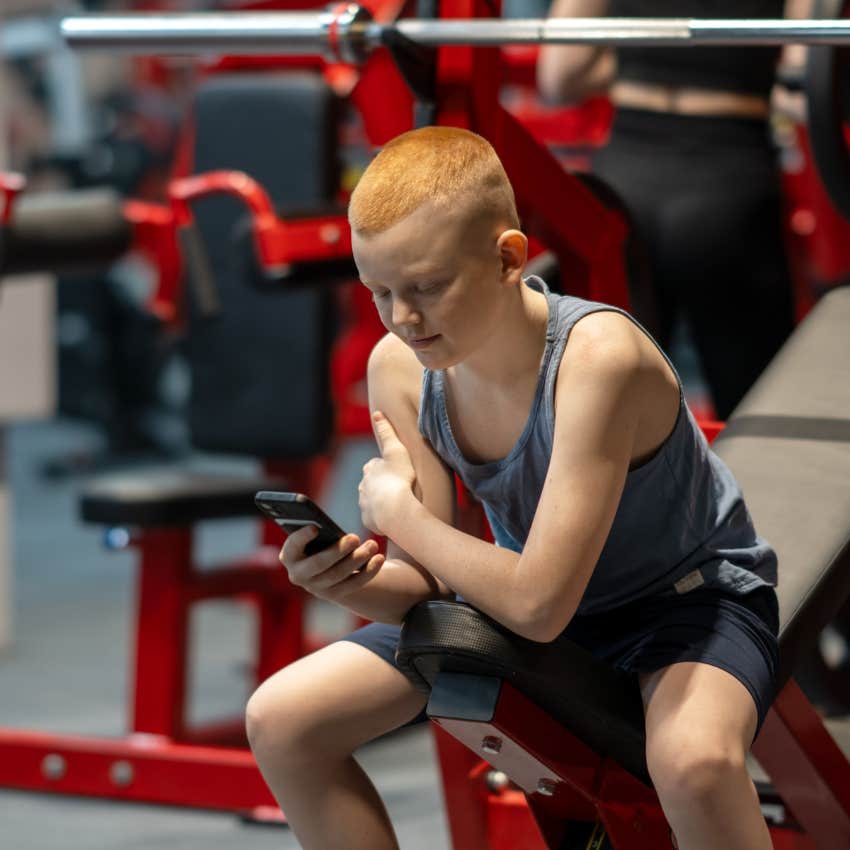 young man in gym watching fitness content on phone feeling insecure