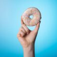 Cropped close up photo of hand rising up tasty donut glazed with sweet cream isolated with bright blue background