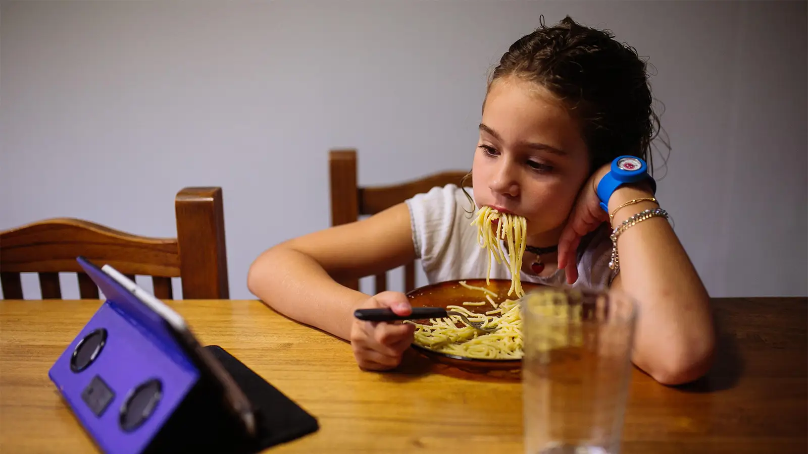 A photo of a girl eating spaghetti while watching a video on a smartphone.