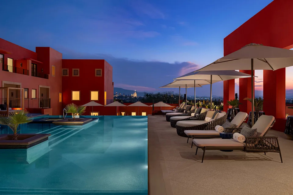 A serene, empty rooftop infinity pool lined with luxury lounge chairs and white umbrellas under a sunset sky at Pueblo Bonito Vantage in San Miguel de Allende, Mexico.