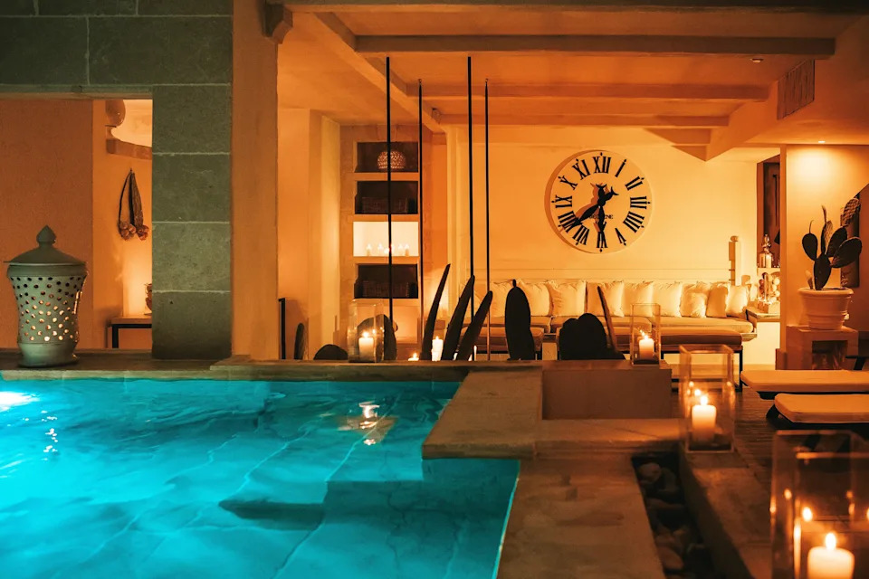 A dimly lit, relaxing indoor pool area and spa lounge illuminated by warm ambient candle lighting at the Canne Bianche Lifestyle Hotel in Puglia, Italy.