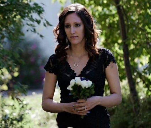 A woman holding flowers walks through a garden.