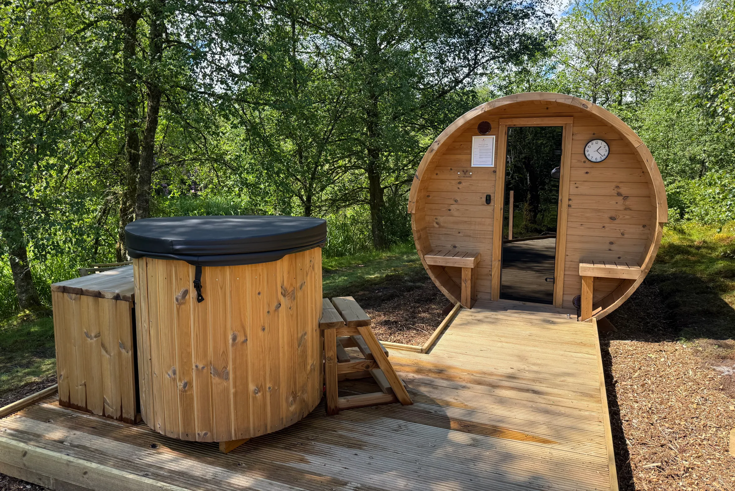 A wooden outdoor sauna and hot tub in a forest setting.