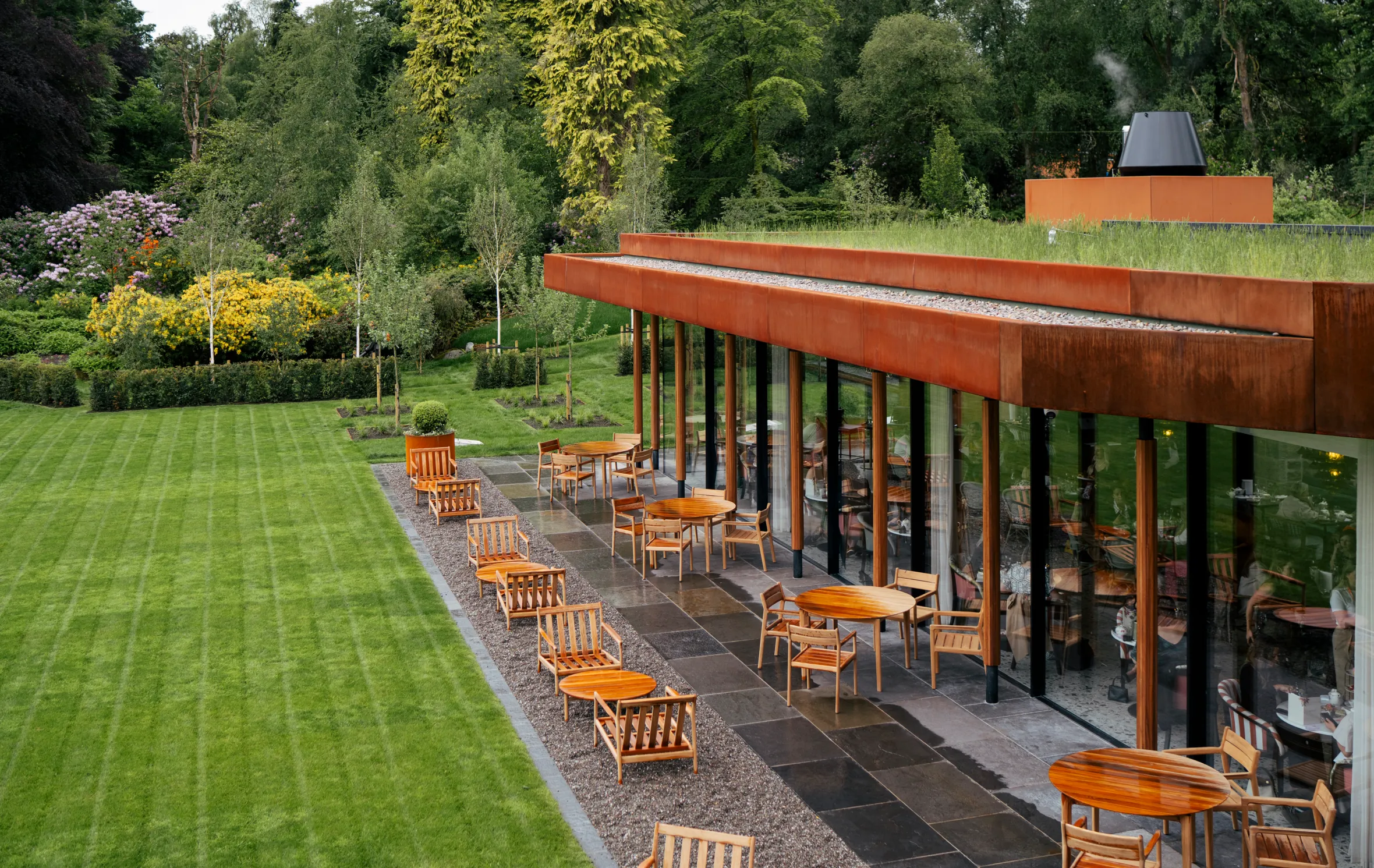 Outdoor dining patio of The Garden Room Restaurant at Cromlix, with a green roof, surrounded by trees and lush gardens.