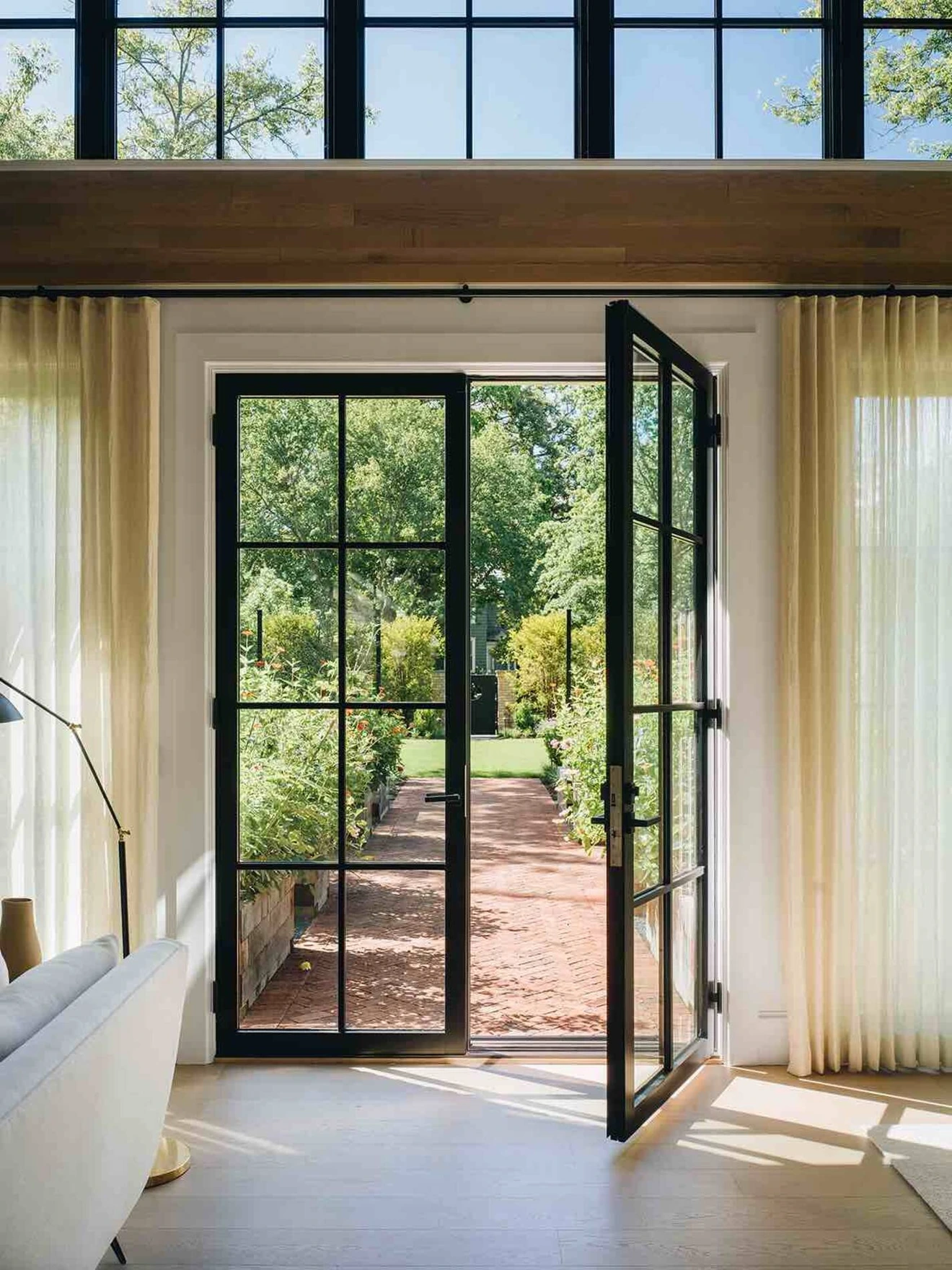Open black-framed glass door leading from bright living room to garden pathway with greenery outside.