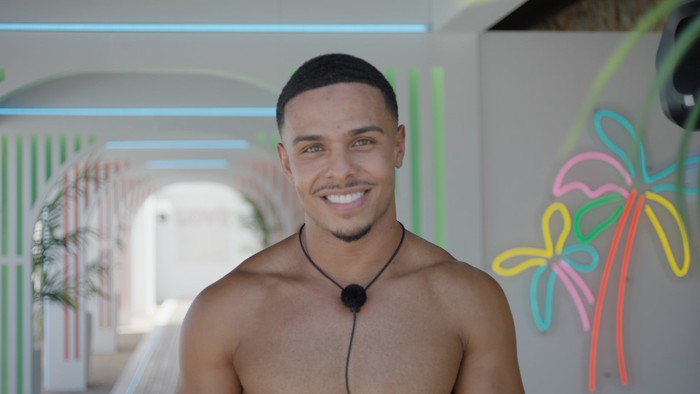Love Island S13 A topless Ethan smiling ahead as he stands in the villa tunnel.