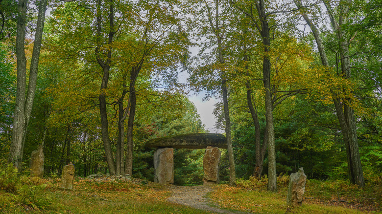 Path leading to a stone arch at Columcille Megalith Park in autumn